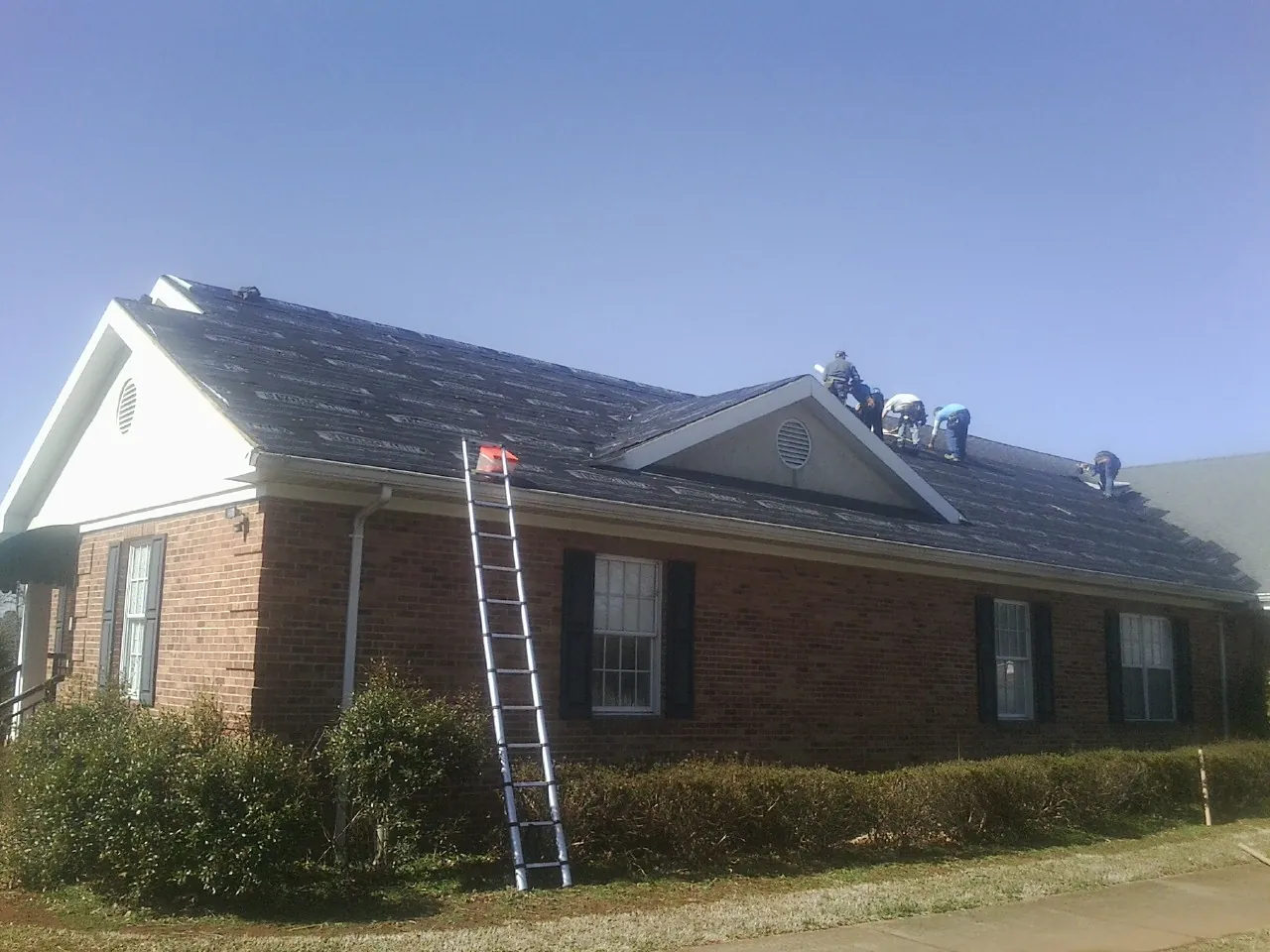 Crew tearing shingles off a brick ranch roof with a ladder set — Emergency Roof Repair work by our crew in Kimballton