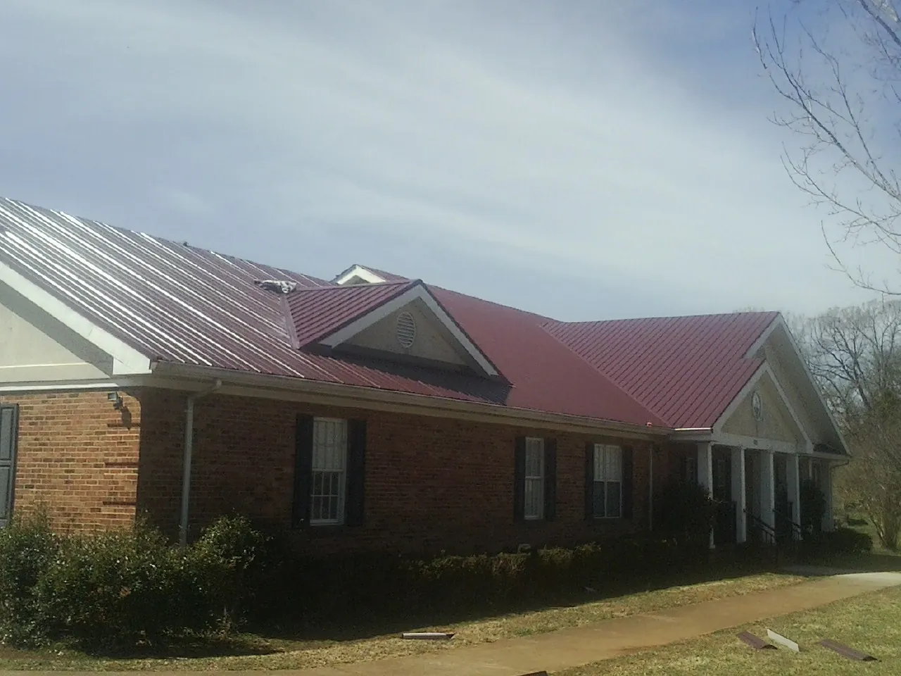 Red metal roof with gabled entries on a long brick building, from a Hail Damage Roof Repair job in Kimballton