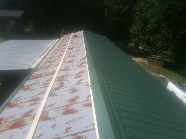 Old rusted panels beside newly installed green metal roofing in Kimballton
