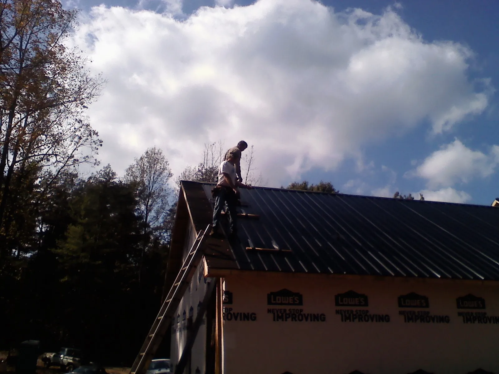 Roofer fastening dark metal panels high against a cloudy sky, from a Roof Inspection job in Kimballton