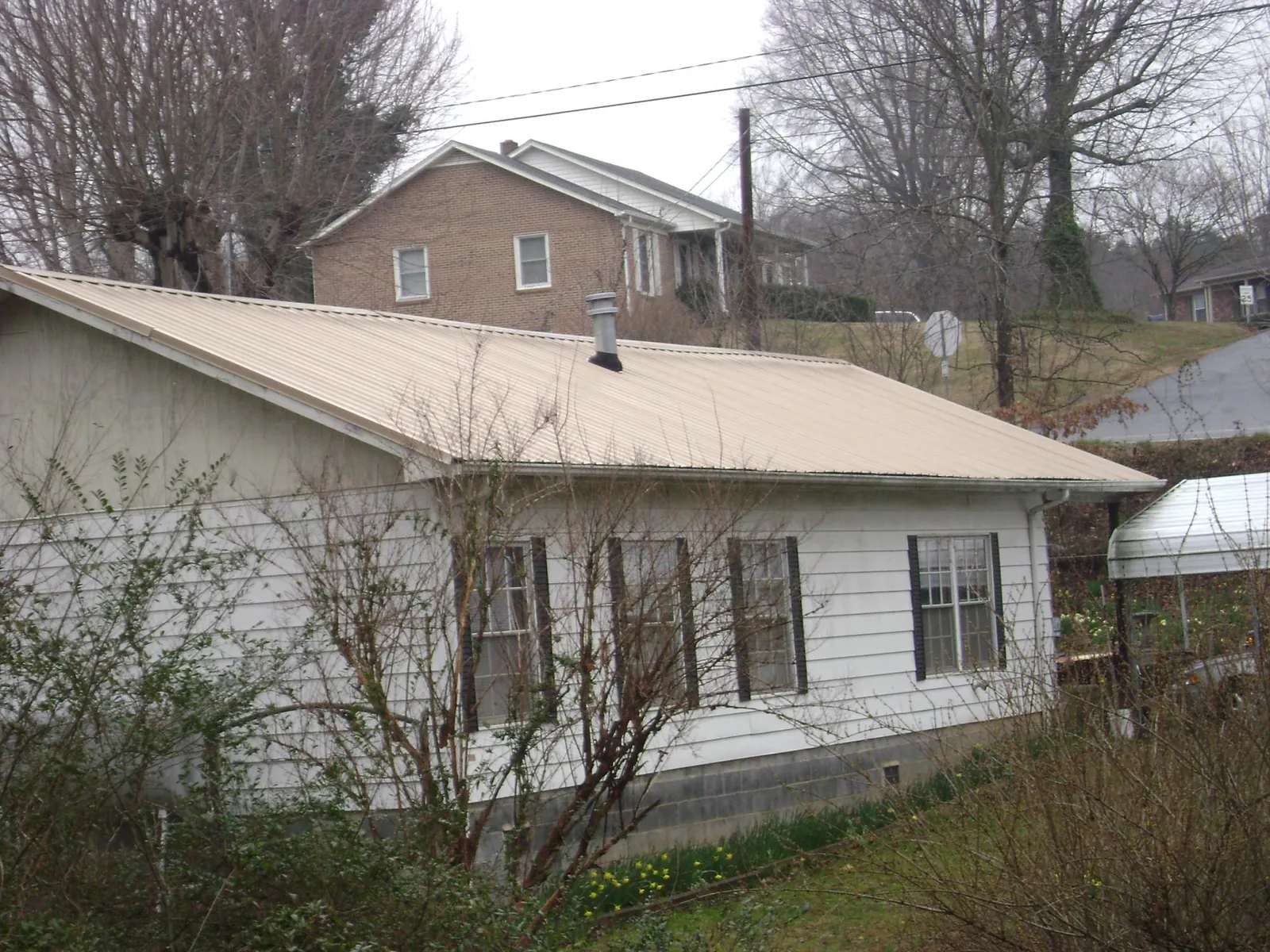 Tan metal roof on a white sided house set into a hillside — Commercial Roofing by Roofing Brothers in Kimballton